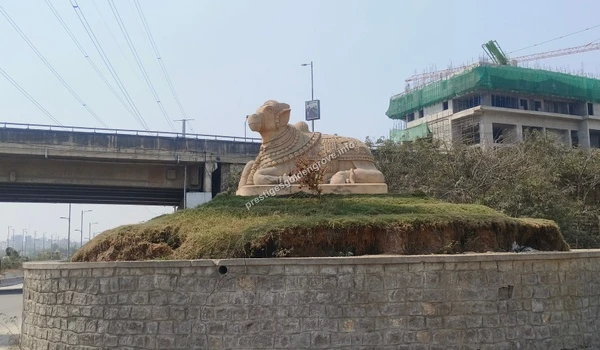 View of a large stone Nandi statue resting on a landscaped traffic island on March 03 , 2026, serving as a prominent navigational landmark near the Nehru Outer Ring Road for Prestige Golden Grove visitors.
